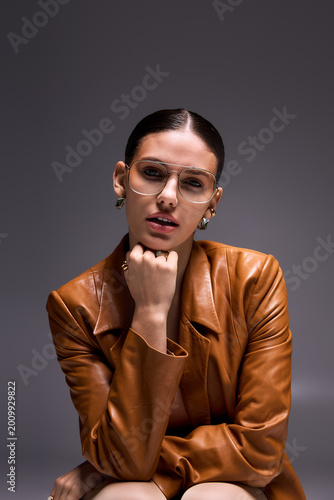 Photos Stylish young woman exudes confidence in leather coat and glasses in studio sett
