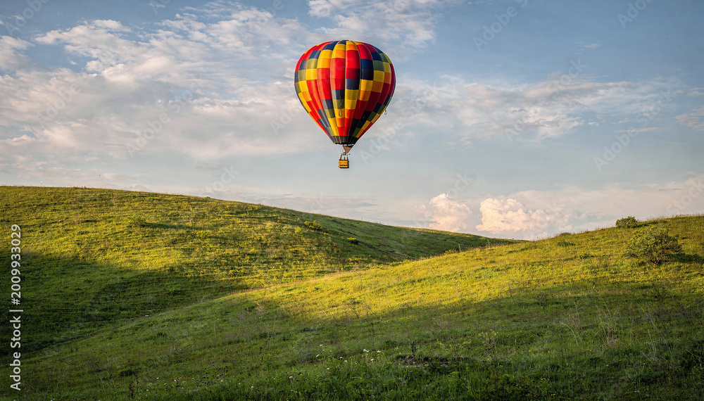 Fototapeta premium Colorful hot air balloon soar over vibrant green hills, summer sky backdrop