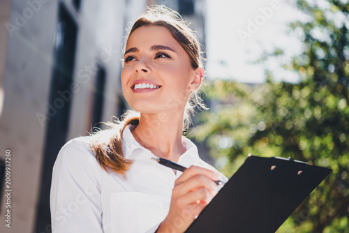 Φωτογραφία Smiling business woman holding clipboard outdoors taking notes — confident young