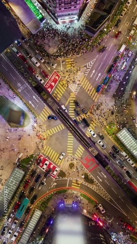Top-down aerial timelapse of a busy intersection in Bukit Bintang, Kuala Lumpur. Crowds crossing streets, moving traffic and colorful city lights create dynamic urban nightlife and motion.