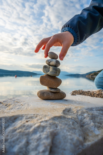 Child Balancing Stones With Right Hand on Seaside With Dramatic Cloudy Sky