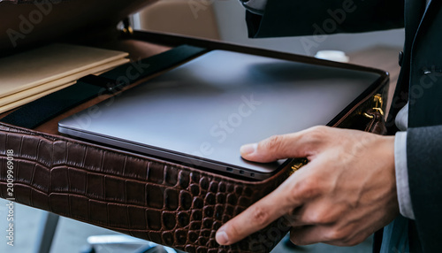 Close-up of a businessman's hands opening a luxury brown crocodile leather briefcase to reveal a sleek laptop.