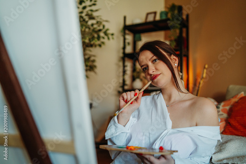 Young woman artist thinking while painting on canvas