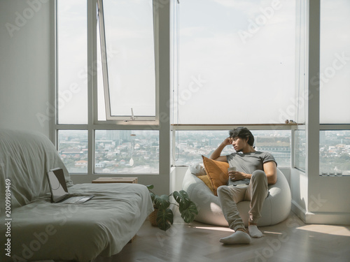 Asian man sitting on the bean bag at the balcony of the condominium, feeling bored and lonely.