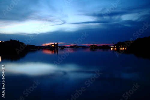 Dreamlike blue hour seascape with sunset reflection and illuminated shoreline at dusk