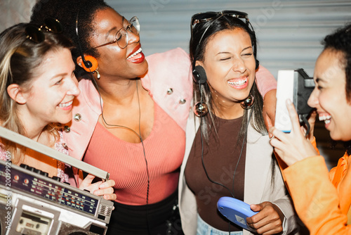 Group of multiracial girls having fun together dancing listening music while taking photo with a vintage instant camera outdoor - Party, nightlife and people lifestyle concept 