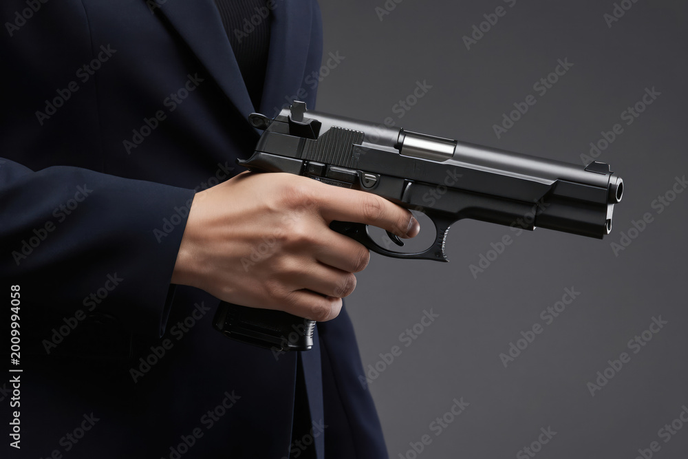 Fototapeta premium A person in a suit holds a handgun. The focus is on the weapon and the hand, suggesting danger or defense. The image evokes themes of power and threat.
