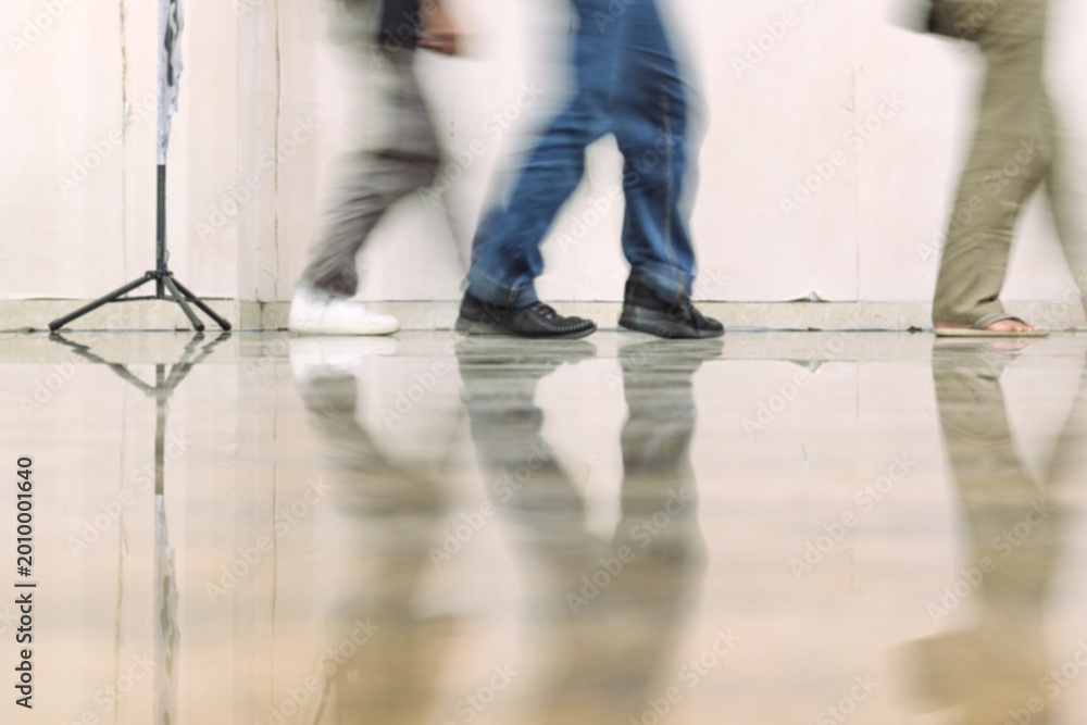 Obraz premium Blurred people walking indoors with floor reflections, dynamic motion and urban lifestyle scene, minimal background, candid perspective