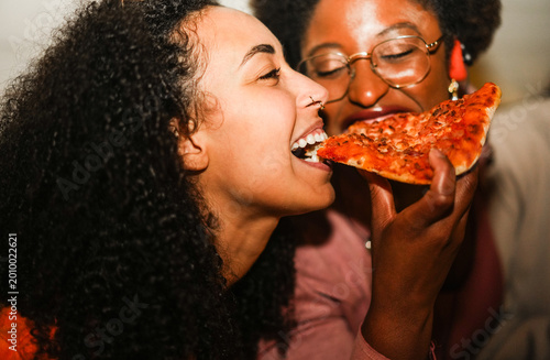 Hungry african american girls eating pizza outdoor in the streets after party concert - Food, people lifestyle  and nightlife concept - Main focus on left woman mouth - UGC flash content