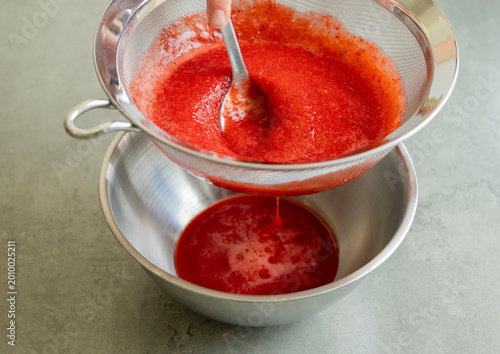 Fotografia Close-up of strawberry puree being strained through a fine-mesh sieve into a bow