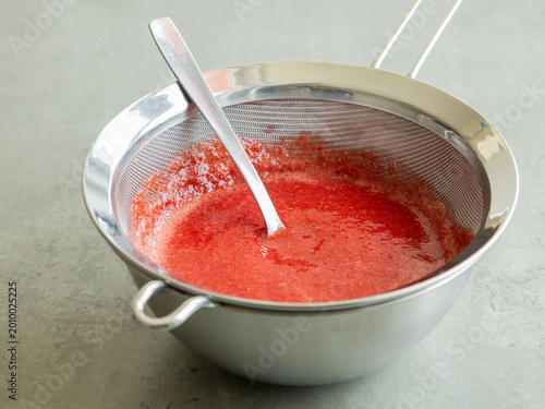 Canvas Print Close-up of strawberry puree being strained through a fine-mesh sieve into a bow