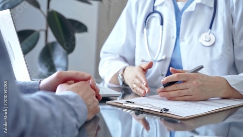 Tableau sur toile Doctor woman wearing white medical coat is consulting patient in clinic office while both are sitting at the glass desk