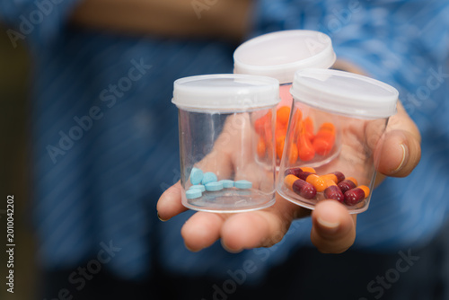 Close-up of a hand holding several small transparent containers filled with different types of pills and capsules. Concept of medication variety