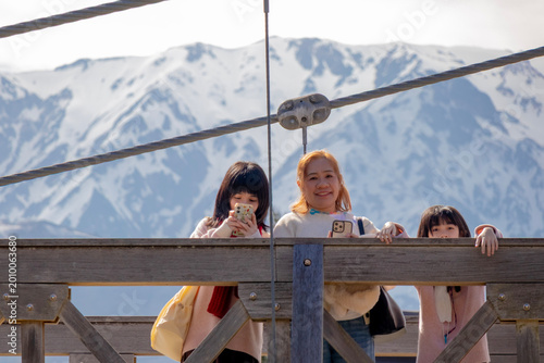 Three Friends on a Suspension Bridge with Snowy Mountains