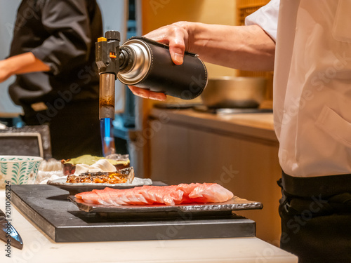 Foto Chef and team using blowtorch to sear fresh sashimi on plate in Japanese restaur