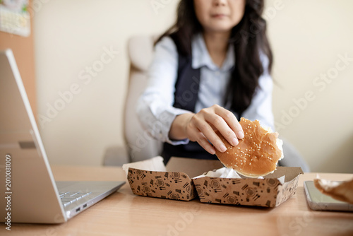 Slika na platnu Asian young businesswoman eating fast food while working in office