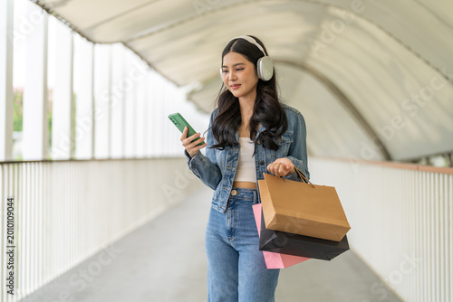 Online shopping, Happy asian woman shopper holding paper bags use smartphone outdoors, Beautiful girl checking online sale promotion, social media on mobile phone in city park, Consumerism lifestyle