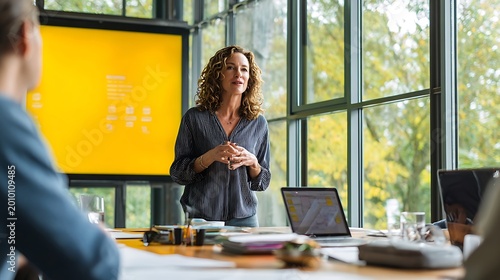 Confident businesswoman presenting ideas to colleagues in a modern office meeting room with large windows.