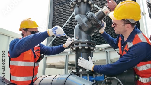 Industrial worker in hard hat and safety vest performing maintenance on large pipes