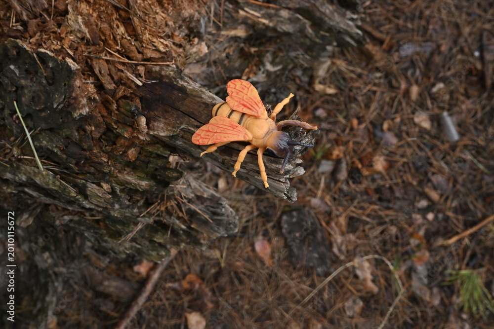 Fototapeta premium Toy insect resembling a bee sitting on a tree stump, illustrating artificial concept life and habitat