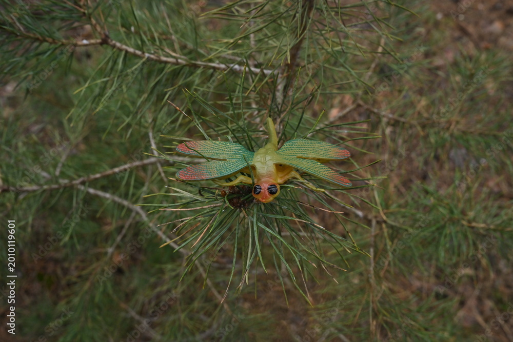 Fototapeta premium Toy dragonfly on a pine branch, blending artificial insect with natural forest environment concept