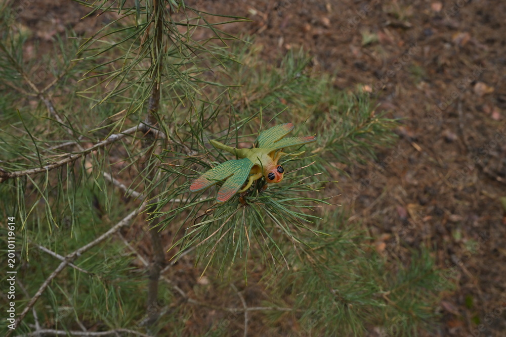 Fototapeta premium Toy dragonfly on a pine branch, blending artificial insect with concept natural forest environment