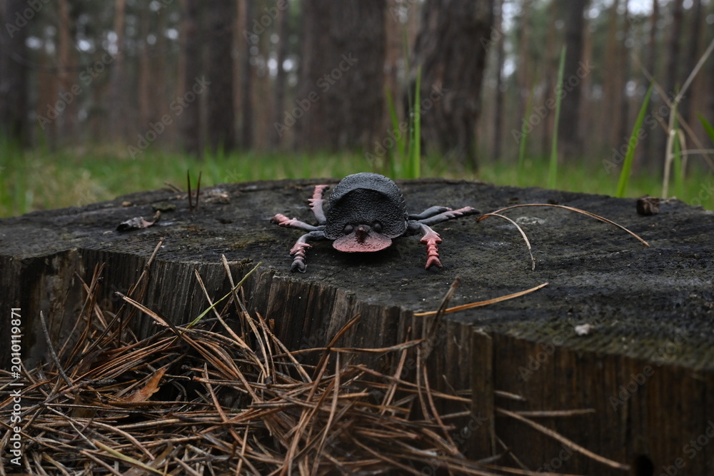 Fototapeta premium Black plastic beetle toy resting on an old tree stump in a forest, contrasting artificial object and natural environment