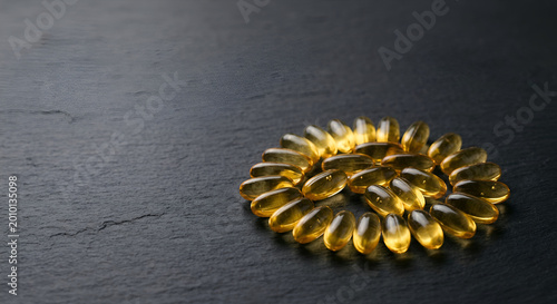 Close-up of a circular arrangement of shiny golden capsules on a dark slate surface with a minimalist aesthetic and rich