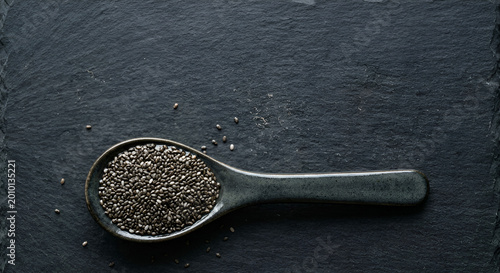 Close-up of a metal spoon filled with small black chia seeds on a dark textured surface emphasizing minimalism and detailed food