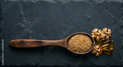 Assortment of flax seeds, walnuts, and oil capsules on a dark slate surface for healthy nutrition and dietary supplements