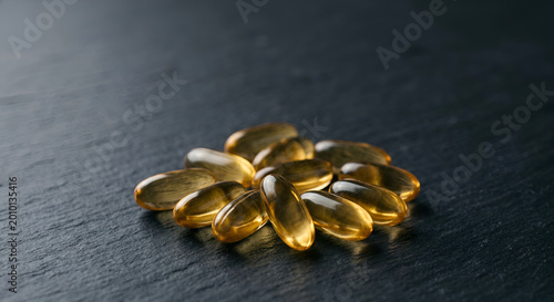 Close-up of golden fish oil capsules arranged on a dark textured surface emphasizing health supplement intake and nutritional