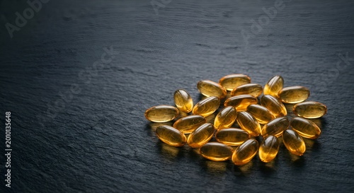 Close-up of softgel capsules with golden-brown hue arranged on a dark textured surface emphasizing dietary supplement