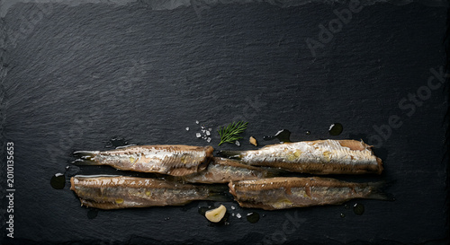 Fresh Sardines on a Dark Slate Serving Plate with Garlic and Herb Garnishes in a Minimalist Presentation