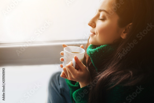 Foto Perfect morning A young brunette woman sits on a windowsill and holds a cup of tea or coffee in her hands