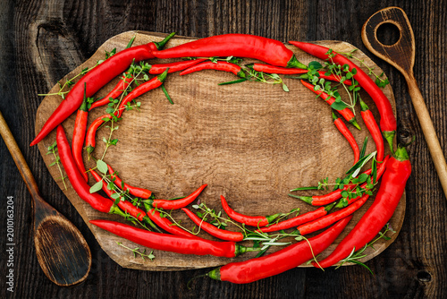 Bild auf Leinwand Fresh red chilies and herbs arranged on a wooden cutting board with cooking uten