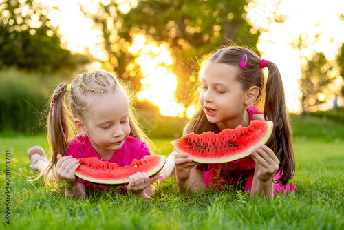 children eating watermelon on a green lawn in summer, two little girls with watermelon in the park in summer, laughing