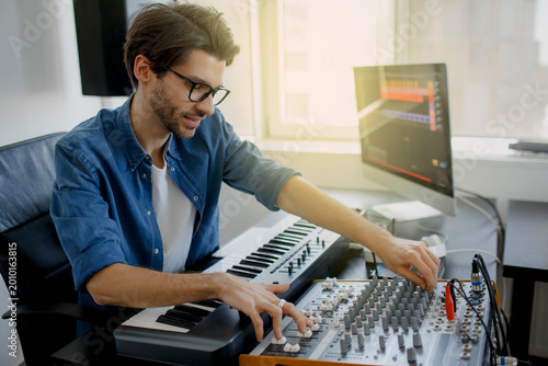 Photography music producer is composing a song on synthesizer keyboard and computer in recording studio
