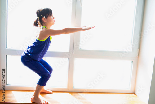 Φωτογραφία Little girl is doing squat exercises workout at home