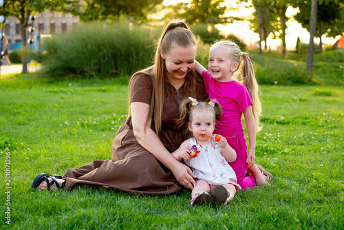 mom and kids walking in the park in summer and having fun, mother and small child hugging on a green lawn, family with two children