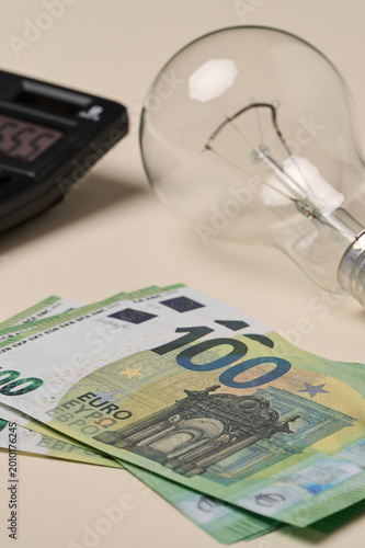 Bills are laid out next to a light bulb and a calculator that shows a number during a work session at home.