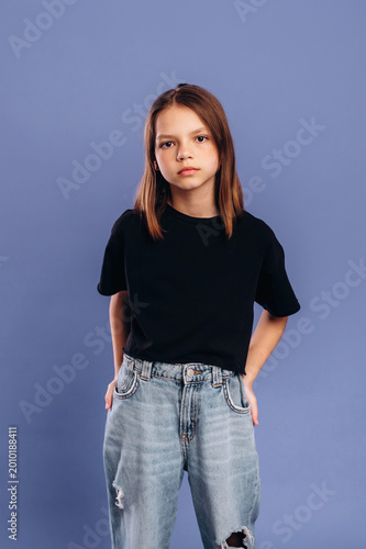 Young girl with medium brown hair wearing a black t-shirt and ripped jeans poses confidently against a solid purple background in a studio setting