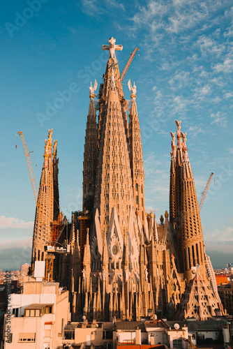 Photography Rooftop view of the Sagrada Familia basilica towers at sunset with the central Jesus Christ tower and cross under a blue sky