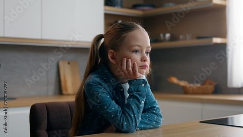 Sad upset pensive thoughtful little offended Caucasian child girl orphan unhappy bad mood lonely kid at home kitchen alone boring stressed daughter sadness family problem domestic violence thinking