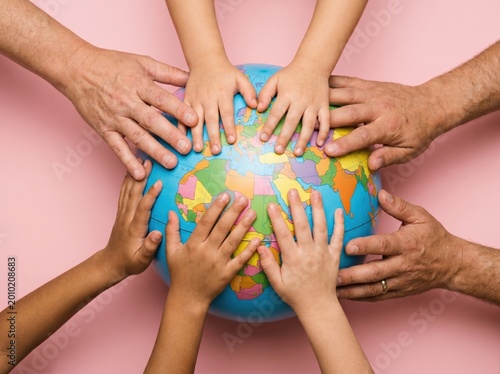 Multiple family hands placed on world globe for educational travel isolated on soft pink background