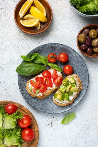 Italian bruschetta with cream cheese, tomatoes, avocado chunks and olives. Table top view