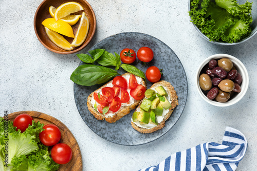 Italian bruschetta with cream cheese, tomatoes, avocado chunks and olives. Table top view