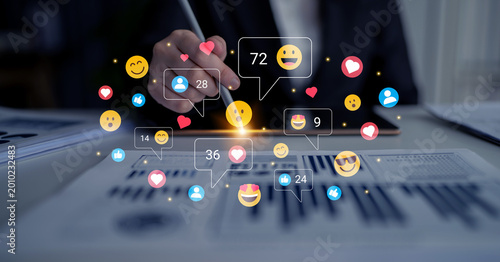 Foto A hand using a smartphone displays emoticons and reactions, showcasing digital engagement in a business environment with documents in view, emphasizing online interaction