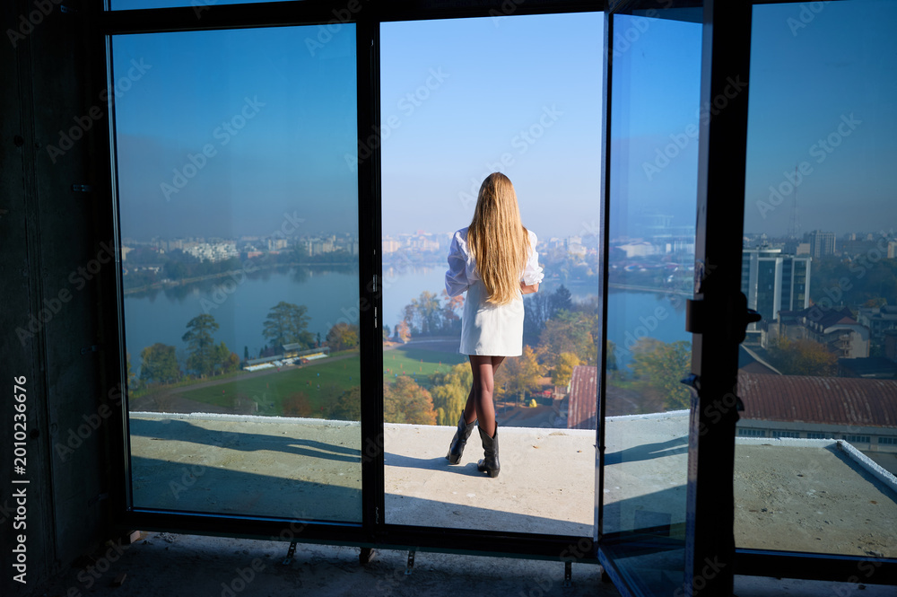 Fototapeta premium Back view of female property manager standing at balcony entrance of unfinished apartment, showing panoramic view. Concept of residential promotion, property launch, business and advertising use
