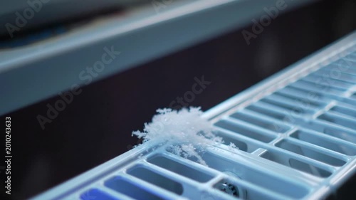Close up side angle view of small white snow crystals resting on top of a gray outdoor metallic grill structure.