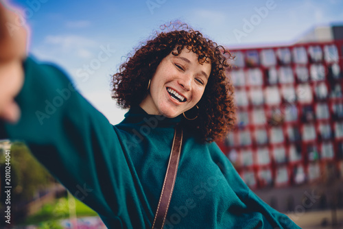 Photos Young woman gestures while filming herself on smartphone, using selfie stick to create content — portraying the freedom and ease of tech use in personal storytelling outdoors